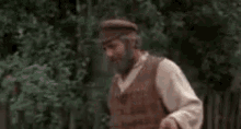 a man with a beard is holding a watering can in front of a wooden fence .