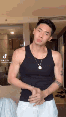 a man wearing a black tank top and white shorts is standing in a room with his hands folded .