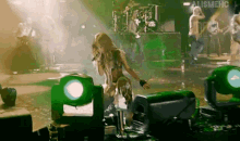 a woman singing into a microphone on a stage with a band behind her and the word alishmehc on the bottom