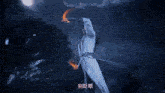 a man in a white robe is standing in front of a full moon surrounded by fire .