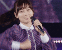 a woman in a purple and white striped shirt is holding a microphone and smiling .