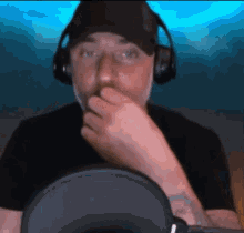a man wearing headphones and a hat is covering his mouth with his hand