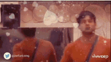 a man in an orange shirt is standing in front of a mirror with snow falling on him