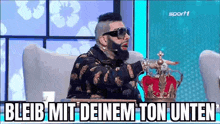 a man with a beard and sunglasses is sitting in a chair wearing a crown and a microphone .