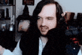 a man with long hair and a beard is talking into a microphone .