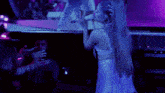 a woman singing into a microphone in front of a crowd with purple lights behind her