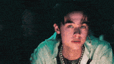 a young man with a pearl necklace around his neck is looking at the camera