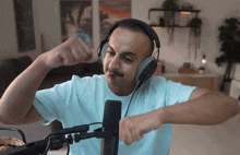 a man wearing headphones flexes his muscles while sitting in front of a microphone