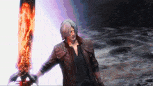 a man in a leather jacket is holding a large sword that is on fire