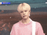 a young man wearing a pink sweater is standing in front of a crowd