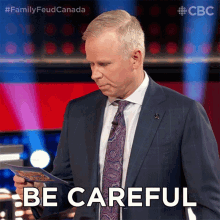 a man in a suit and tie holds a piece of paper and says be careful