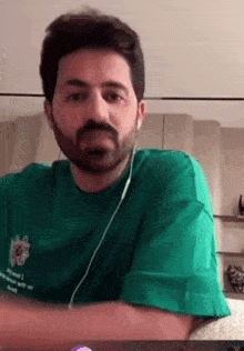 a man with a beard is wearing a green shirt and earbuds .