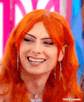 a woman with red hair is wearing a necklace and hoop earrings and smiling .