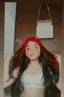 a woman with red and black hair is holding her hair in front of a door .