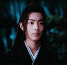 a young man with long hair and a red flower in his hair is wearing a kimono .