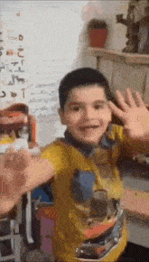 a young boy in a yellow shirt is giving a high five to someone .