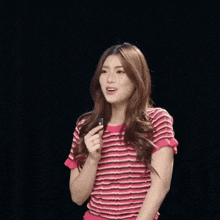 a woman in a pink and white striped shirt is holding a small object in her hand