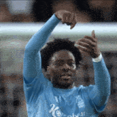 a soccer player in a blue shirt is giving a thumbs up while standing on the field .