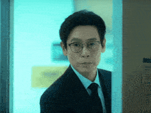 a man wearing glasses and a suit is standing in front of a door