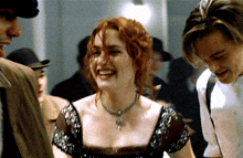 a woman with red hair and a necklace smiles while standing next to two men