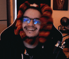 a man wearing glasses and a scarf on his head is smiling in front of a microphone