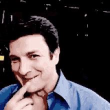 a man in a blue shirt is covering his mouth with his hand .