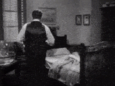 a black and white photo of a man in a suit standing next to a bed