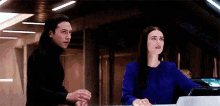 a man and a woman are standing next to each other in a room . the woman is wearing a blue top .
