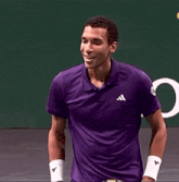 a man wearing a purple adidas shirt holds his hand to his face