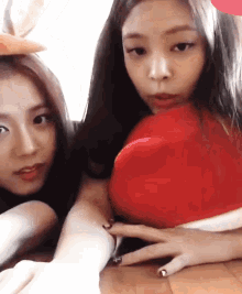 two girls are sitting next to each other and one is holding a red heart