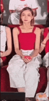 a woman in a red tank top and white pants is sitting on a red couch with other people .