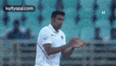 a man in a white shirt is standing in front of a stadium with his hands in the air .