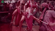 a group of people are dancing in a crowd while a man holds a stick .
