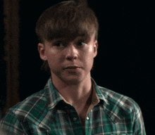 a young boy in a green plaid shirt is looking at something