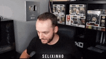 a man in a black shirt is sitting in front of a shelf full of funko pop figures and says " selixinho "