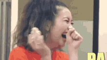 a woman in a red shirt is laughing with her hands over her mouth .
