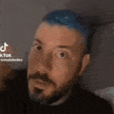a man with a beard and blue hair is making a funny face
