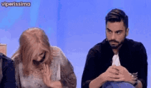 a man and a woman are sitting next to each other in front of a blue wall .