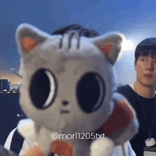 a man is holding a stuffed animal that looks like a cat with big eyes .