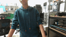 a boy wearing a blue hoodie stands in front of a desk with a shelf that says ' a '
