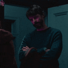 a man in a blue sweater stands with his arms crossed in front of a door