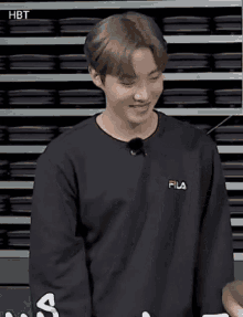 a young man wearing a black fila sweatshirt is standing in front of a shelf .