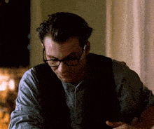 a man wearing glasses and a vest is looking down at something