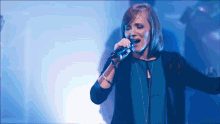 a woman singing into a microphone while wearing a blue shirt