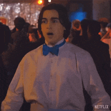 a man in a tuxedo with a blue bow tie is standing in a crowd of people .