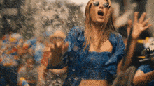 a woman in a blue crop top and sunglasses is dancing in the rain