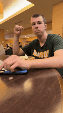 a man wearing a mason shirt sits at a table with food