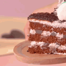 a person is holding a slice of chocolate cake on a wooden cutting board
