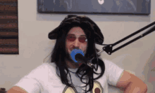 a man wearing a wig and sunglasses is standing in front of a microphone with a blue object in his mouth .