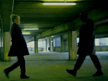 a man and a woman walk in a dark parking garage